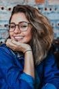 A young woman wearing glasses and denim, smiling in an indoor setting.